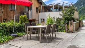 An outdoor patio with a table and chairs, a red umbrella, and a wooden building with a balcony.
