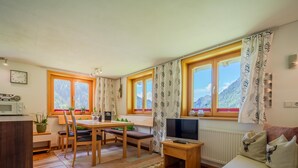 A cozy living room with a sofa, a TV, a dining table with chairs, and a kitchen area with a microwave.