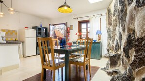 A modern kitchen with a dining area, wooden chairs, a glass table, and a stone wall. - Rustic Home with Gorgeous Pool Area, Terrace, Private Patio, Wi-Fi and Grill (Mozaga)