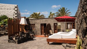 A stone building with a wooden gate, a red umbrella, and a lounge chair. - Rustic Home with Gorgeous Pool Area, Terrace, Private Patio, Wi-Fi and Grill (Mozaga)