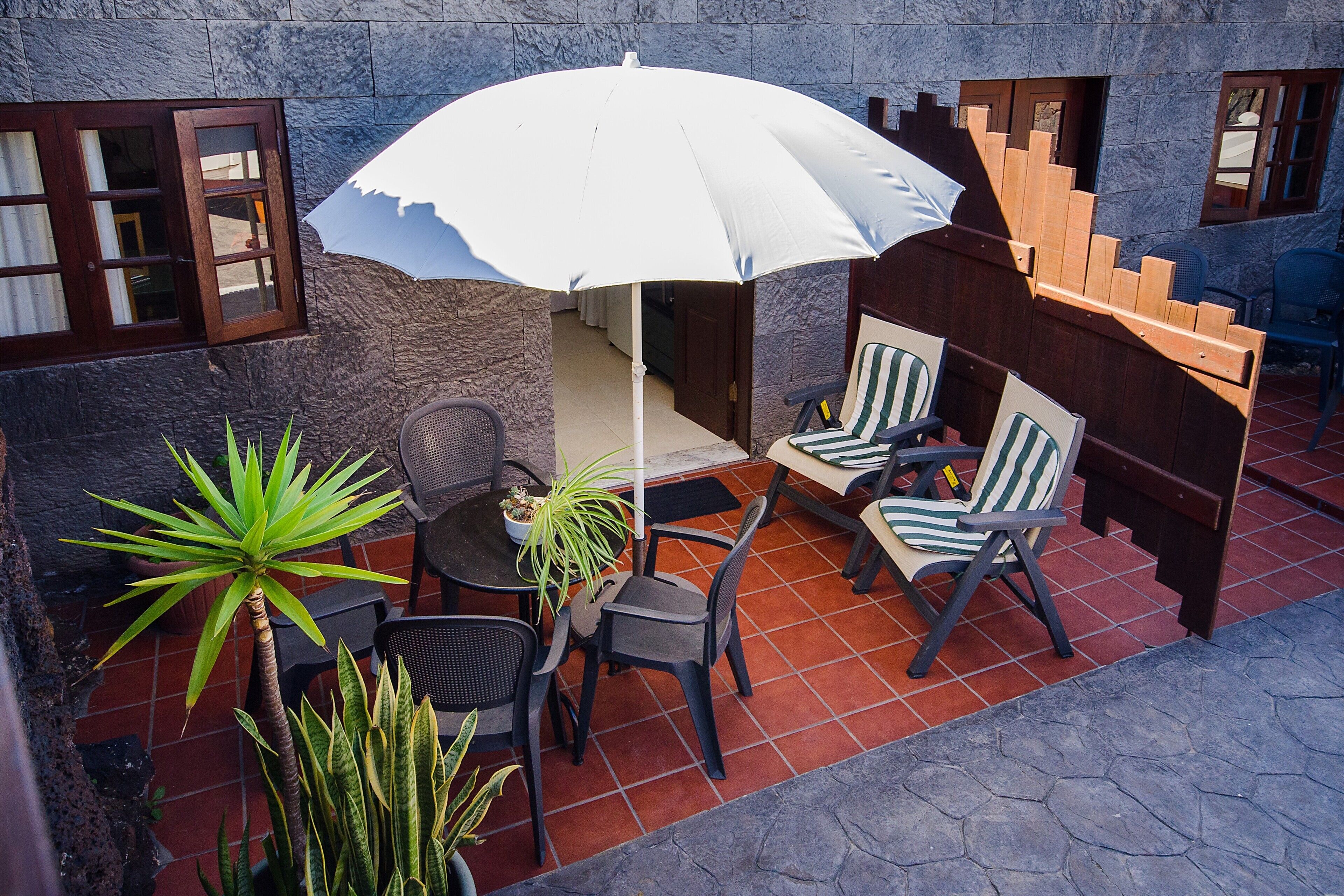 An outdoor patio with a table and chairs, a white umbrella, and potted plants.