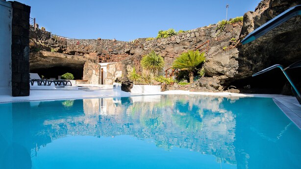 A clear blue pool with a rocky backdrop, a small waterfall feature, and a stone pathway leading to a seating area. - Rustic Home with Gorgeous Pool Area, Terrace, Private Patio, Wi-Fi and Grill (Mozaga)