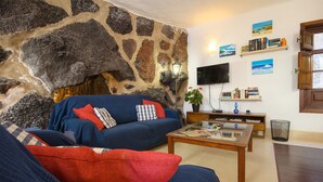 A living room with a stone wall, a blue sofa, a wooden coffee table, and a television on the wall. - Rustic Home with Gorgeous Pool Area, Terrace, Private Patio, Wi-Fi and Grill (Mozaga)