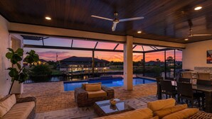 Un espace extérieur abrité comprenant une piscine, des sièges et une vue sur un coucher de soleil sur l’eau.