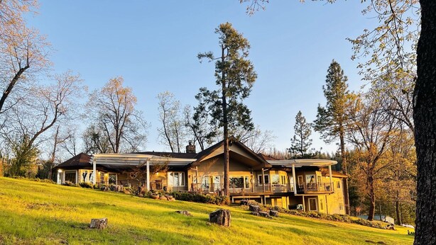 A large, two-story house with a covered porch and multiple windows, surrounded by a grassy landscape and trees. - 80-acre Mountaintop Villa with Spectacular Views (Coarsegold)