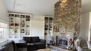 A cozy living room with a stone fireplace, a large bookshelf, and a comfortable seating area. - 80-acre Mountaintop Villa with Spectacular Views (Coarsegold)
