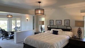 A bedroom with a large bed, bedside lamps, a desk with a chair, and a window with a view of greenery. - 80-acre Mountaintop Villa with Spectacular Views (Coarsegold)