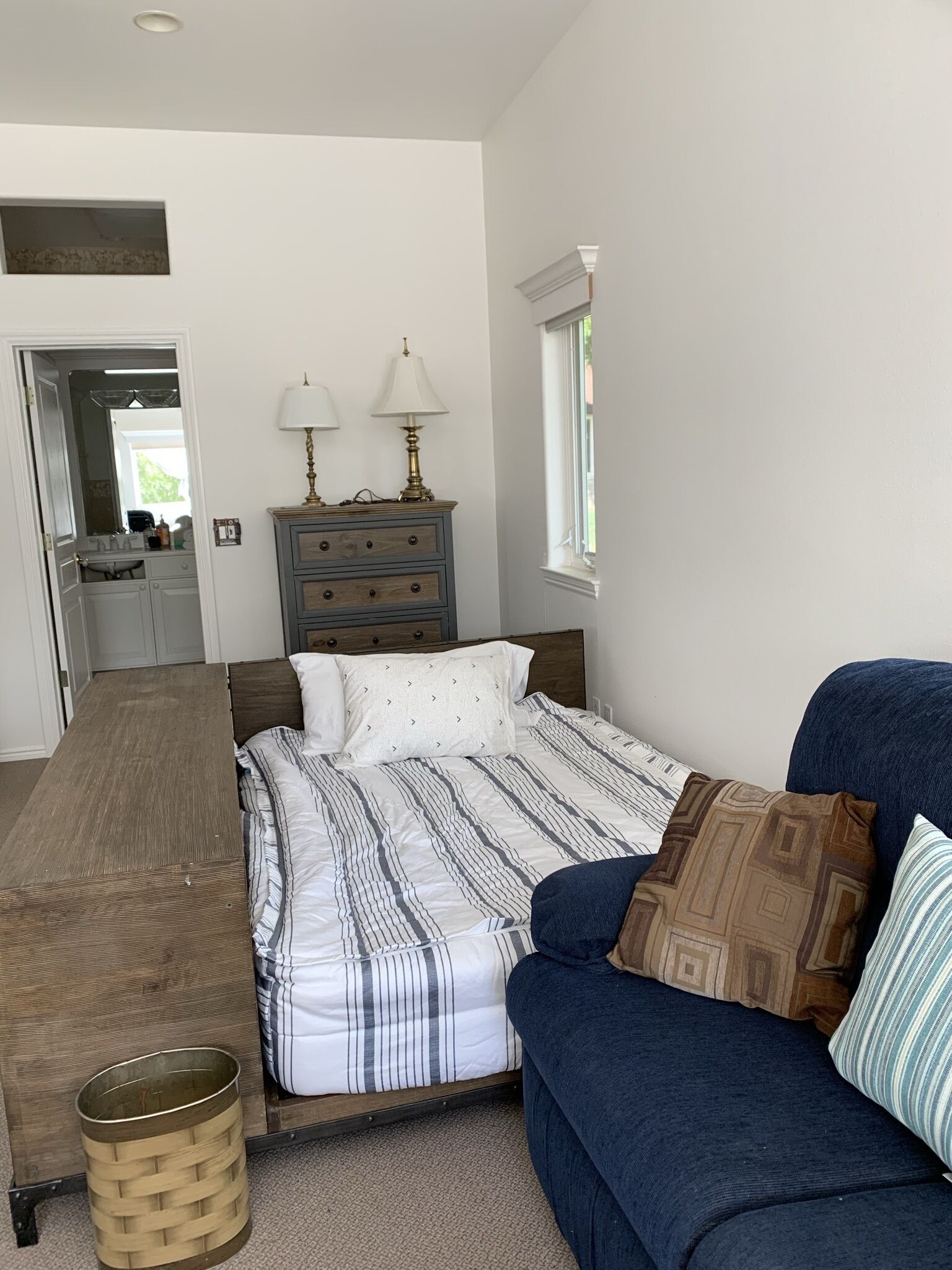 A bedroom with a bed, a dresser, a blue sofa, and a window.