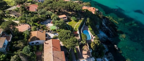 An aerial view of a coastal residential area with houses, a swimming pool, and a beach.