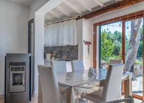 A dining area with a table and chairs, a stove, and a view of greenery outside.