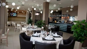 A restaurant with round tables and chairs, a bar area, and a television screen. - Hotel Vila Lule (Durrës)