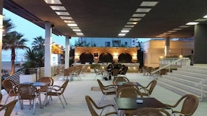 An outdoor cafe area with wicker tables and chairs, a bar area with a counter, and a staircase leading to an upper level. - Hotel Vila Lule (Durrës)