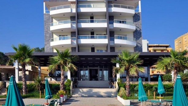 A multi-story hotel with a central entrance, balconies on each floor, and a surrounding garden with palm trees and umbrellas. - Hotel Vila Lule (Durrës)