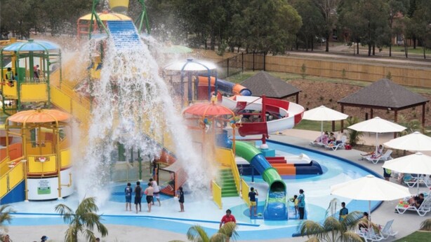 Un parc aquatique doté d’un grand toboggan aquatique, de nombreuses aires de jeux et d’un espace piscine avec des chaises longues et des parasols.