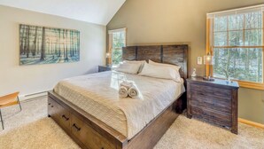 Une chambre avec un grand lit, une tête de lit en bois, une table de chevet, un bureau, une chaise et un tableau accroché au mur.