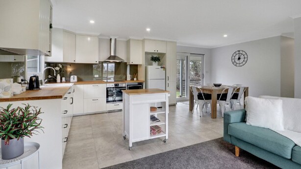A modern kitchen with white cabinets, a central island, and a dining area with a table and chairs. - Katta Cottage (Mansfield)
