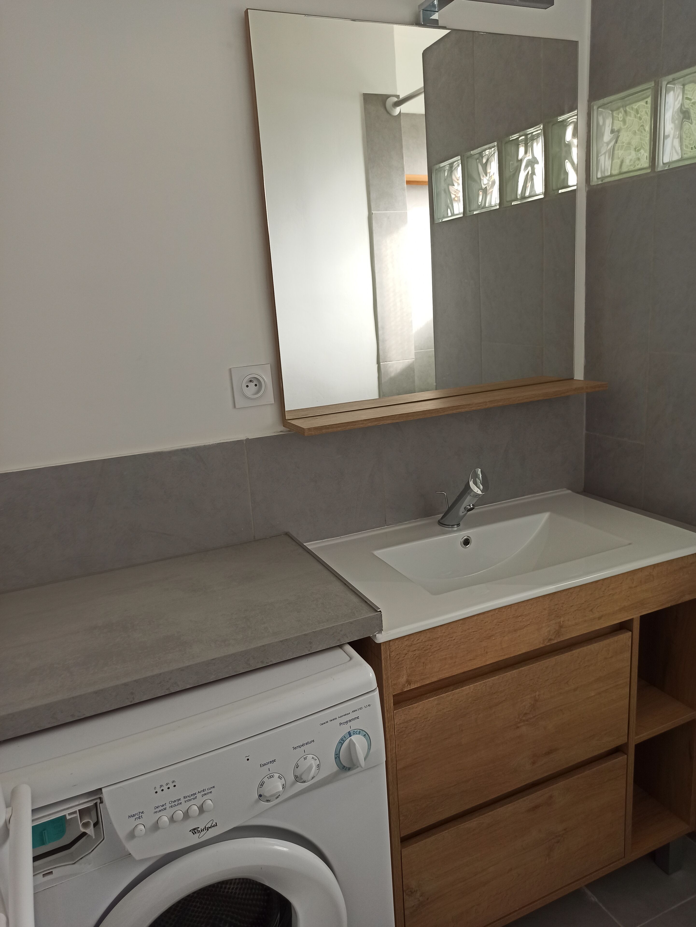 A modern bathroom with a built-in washing machine, a sink, and a mirror.