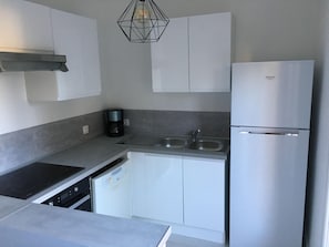 A modern kitchen with white cabinets, a built-in dishwasher, a stainless steel refrigerator, and a coffee maker. - Logement Entier, cap D'agde, 6 Pers, 100m Plages, Falaises (Agde)