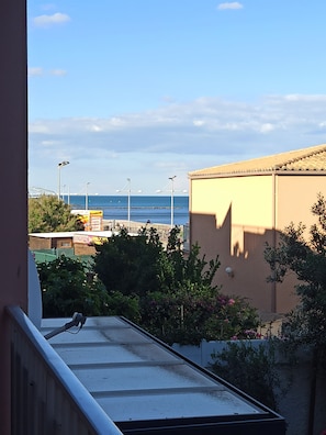 A view from a balcony overlooking a beach with a clear sky, a building with a tiled roof, and some greenery. - Logement Entier, cap D'agde, 6 Pers, 100m Plages, Falaises (Agde)