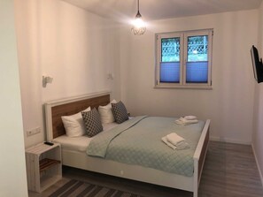 Ein Schlafzimmer mit einem Bett, einem Nachttisch, einem Fenster mit Jalousien und einer Pendelleuchte.