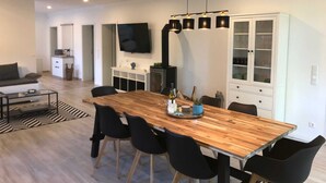 Un espacio habitable moderno con una mesa de comedor de madera, sillas negras, un televisor montado en la pared y un mueble con puertas de vidrio.