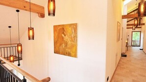 A staircase with wooden railings and hanging pendant lights, leading to a room with a large abstract painting on the wall.