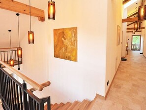 Un escalier avec des rampes en bois et des luminaires suspendus, menant à une pièce où un grand tableau abstrait orne le mur.