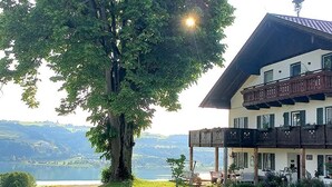 A building with a balcony, a tree in front, and a view of a lake.