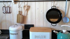 A kitchen with a white wall, a black pot, a white compost bin, and a wooden box labeled 'BROTLIEBE'.