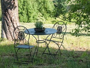 Een ronde metalen tafel met twee stoelen, een bloempot en een boom op de achtergrond.