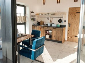 Une cuisine compacte avec des meubles en bois, un coin repas agrémenté d’une chaise bleue et une porte vitrée donnant sur un balcon.