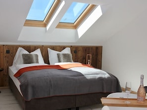 A bedroom with a skylight, a bed with pillows, a bedside table with a bottle and glass, and a wooden headboard.