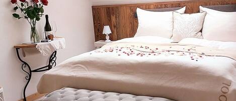 Un dormitorio con una cama, un banco, una mesita de noche, una lámpara y un florero con flores.