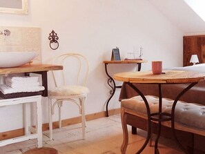 Una habitación acogedora con una silla blanca, una mesa redonda con una taza roja, un banco de madera y un armario blanco.