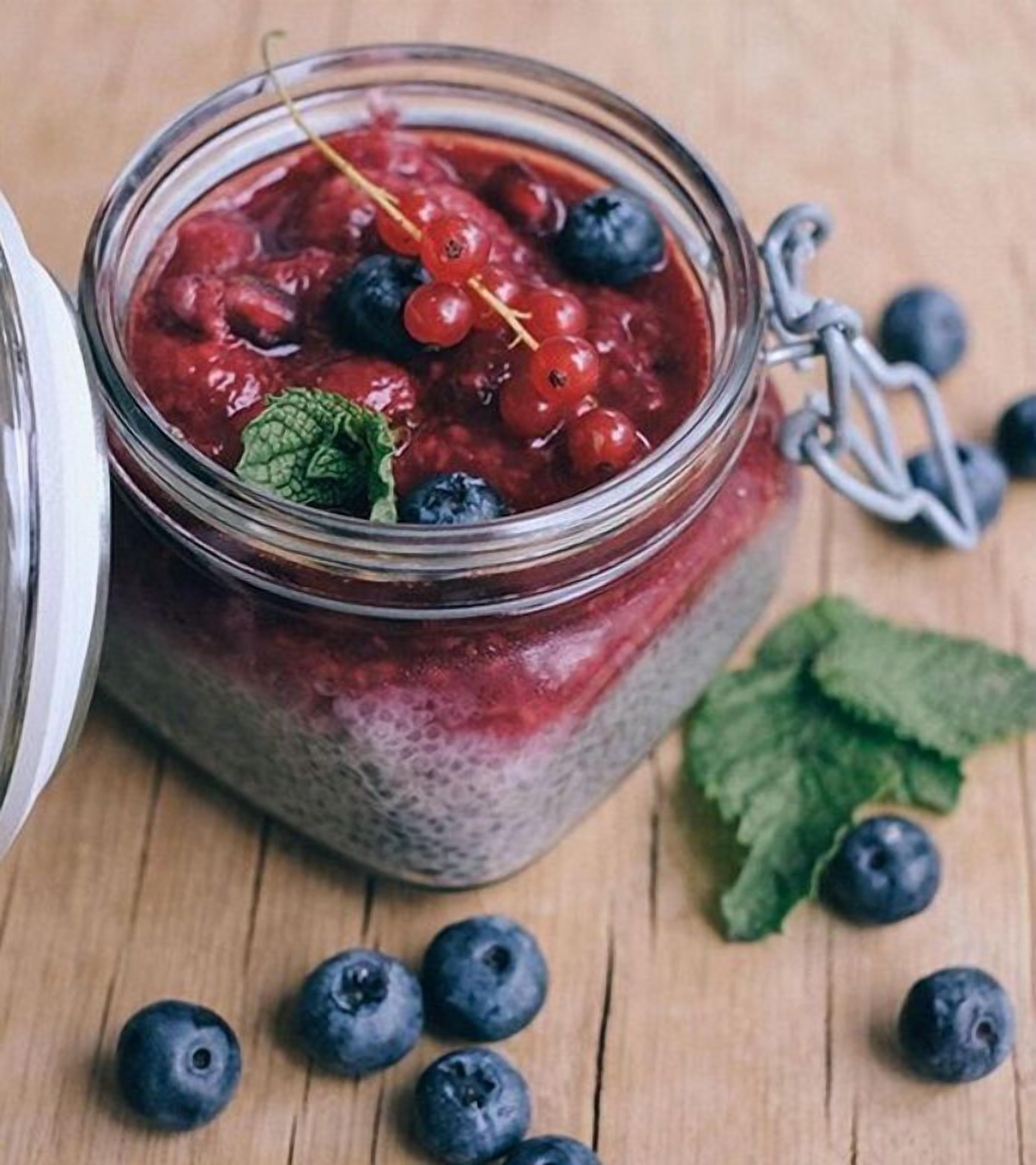 Ein Glas Beerenkompott mit Blaubeeren und Rote Johannisbeeren, umgeben von losen Blaubeeren und Minzblättern auf einer Holzoberfläche.