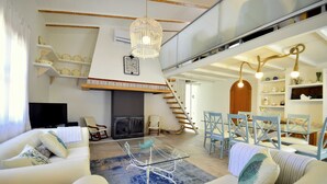 En moderne stue med et sofabord i glas, hvide sofaer, en pejs og en trappe til en etage ovenover.