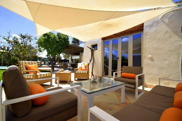 An outdoor patio with cushioned seating, a glass table, and a large umbrella providing shade.