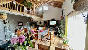 A spacious living area with a wooden dining table, chairs, and a TV. There are potted plants and a balcony with wooden railings. - Large atypical house in the Basque country, sleeps 16. Indoor pool (Ayherre)