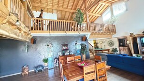 A spacious living area with a high ceiling, wooden balcony, and a dining table set with chairs. - Large atypical house in the Basque country, sleeps 16. Indoor pool (Ayherre)