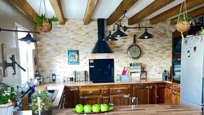 A kitchen with a stone wall, wooden beams, hanging plants, a central island with green apples, and a refrigerator with magnets. - Large atypical house in the Basque country, sleeps 16. Indoor pool (Ayherre)