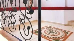 A hallway with a decorative metal railing, a patterned floor, and framed artwork on the walls. - Umut Denizi Konukevi (Bozcaada)