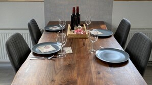 Une table à manger dressée pour quatre personnes, avec des bouteilles de vin, des verres et un plateau en bois.