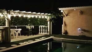 An outdoor pool area with string lights, a pergola, and a small table with chairs. - Le Pastre (Montpeyroux)