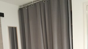 A room with a large grey curtain, a wooden bed, and a mirror on the wall. - Le Pastre (Montpeyroux)