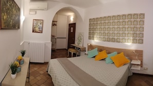 Habitación de hotel con cama, escritorio, silla y una mesita con planta en maceta.