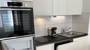 Ett modernt kök med en inbyggd ugn, en kaffebryggare och en diskho i rostfritt stål.