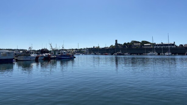 En hamn med förtöjda båtar, en klar himmel och byggnader i bakgrunden.