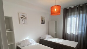 Ett sovrum med två enkelsängar, en garderob, en hängande lampa och ett fönster med gardiner.