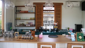 A kitchen with wooden cabinets, a countertop with various kitchen items, hanging pendant lights, and a window with wooden shutters. - Liberta Malioboro South (Yogyakarta)
