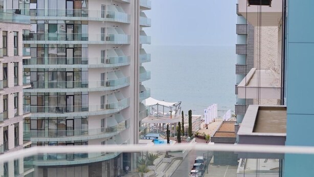 Un edifici alt amb múltiples balcons, un aparcament i vista al mar.